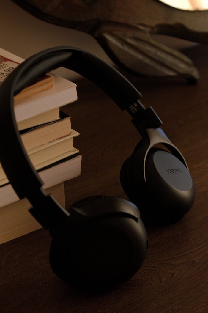 Close-up of stylish black wireless headphones beside stacked books on a wooden table.